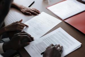 Two individuals reviewing and signing official documents in an indoor setting.